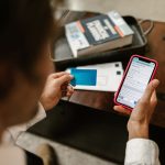 Pessoa realiza um pagamento online usando um smartphone e um cartão de crédito em ambiente interno.