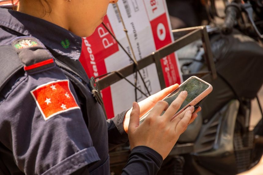 Agente policial uniformizada usa um smartphone ao ar livre em Londrina, no Paraná.