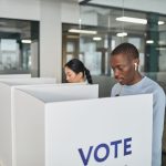 Duas pessoas votam em uma cabine de votação em um local fechado.