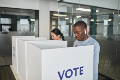 Duas pessoas votam em uma cabine de votação em um local fechado.