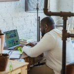 Freelancer trabalha concentrado em um computador portátil diante de uma mesa de madeira.