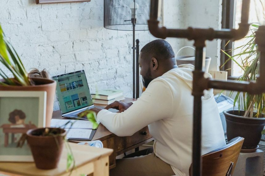 Freelancer trabalha concentrado em um computador portátil diante de uma mesa de madeira.