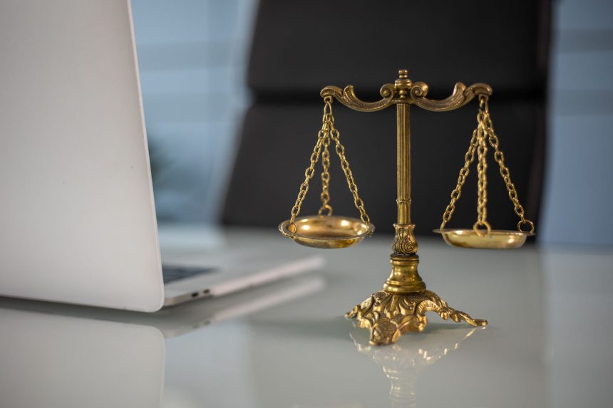 Balanças douradas da Justiça sobre uma mesa, ao lado de um laptop.